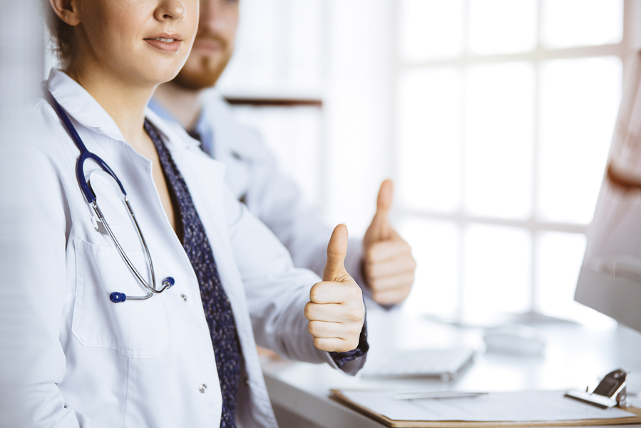 Two doctors sitting with thumbs up in hospital office. Medical help, countering viral infection concept